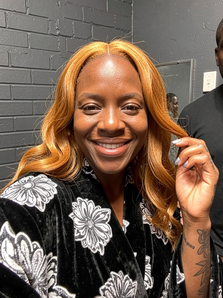 Mão segurando mecha de cabelo ruivo dourado ao lado de pele morena.