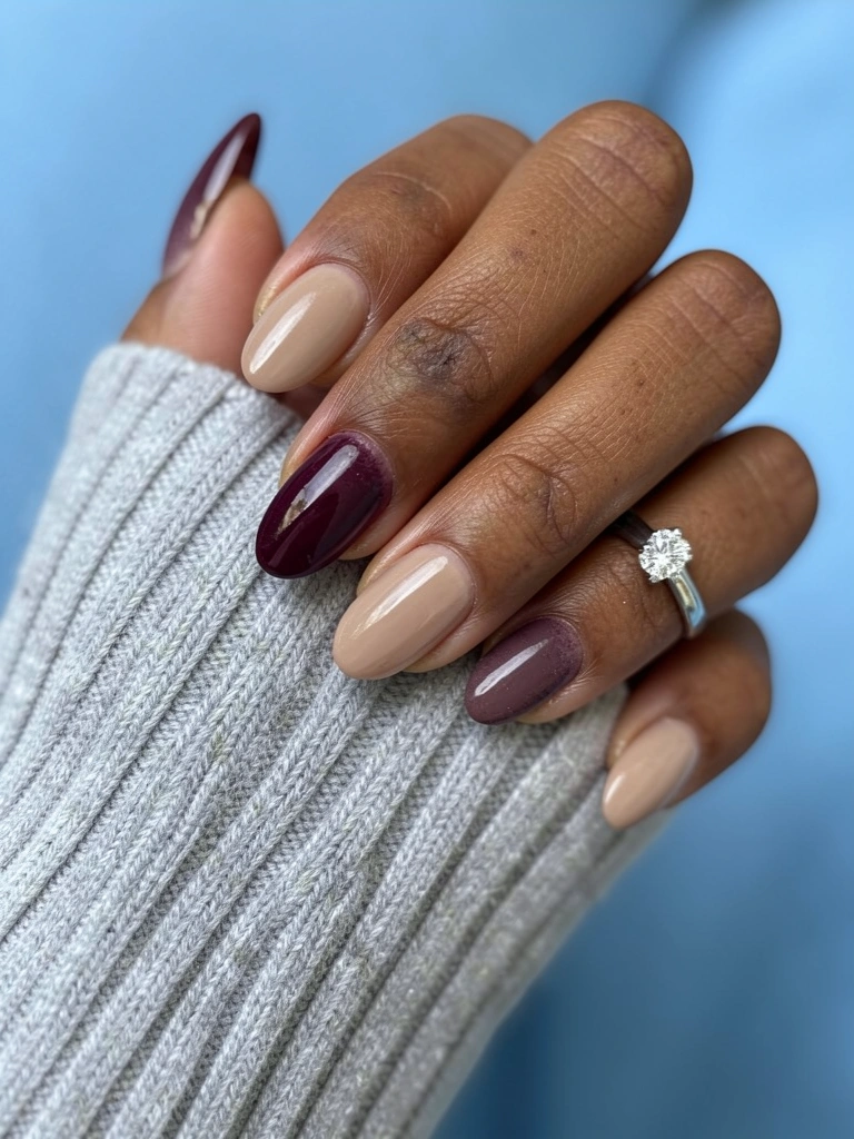 Mão morena com esmalte nude e berinjela, fundo neutro.