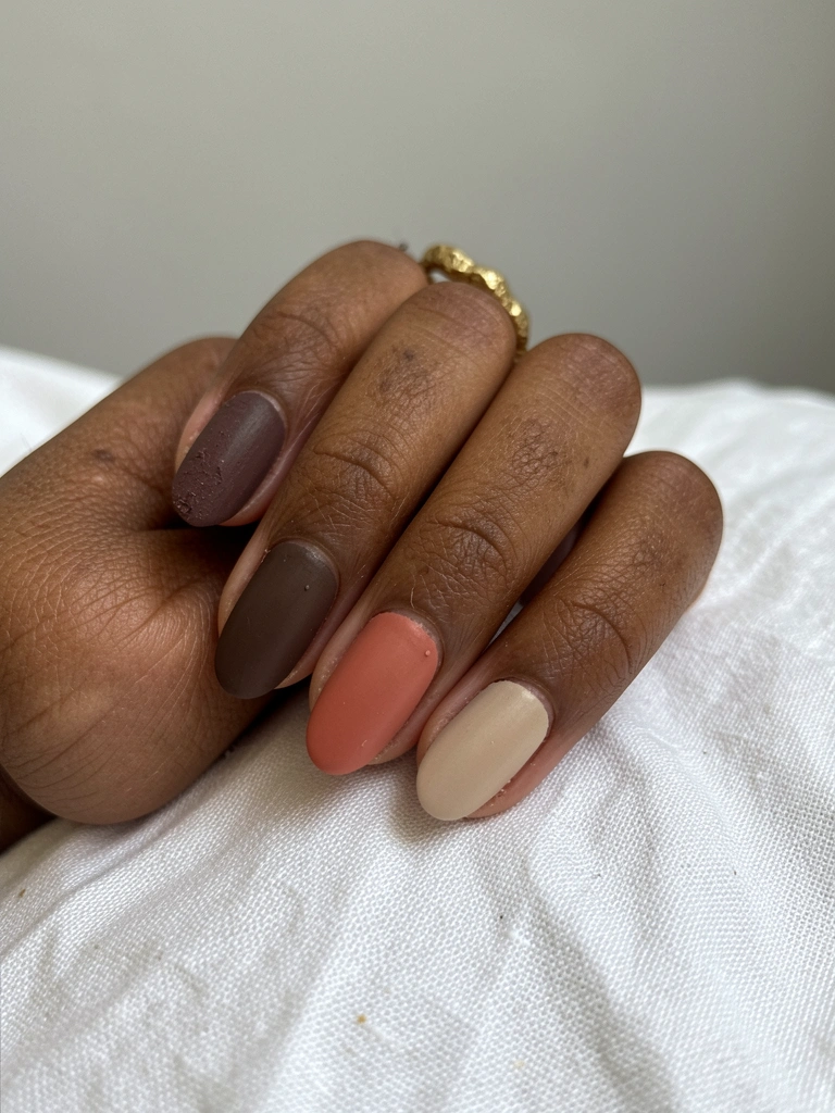 Mãos femininas com unhas foscas em tons de azul, rosa e nude sobre fundo cinza claro.