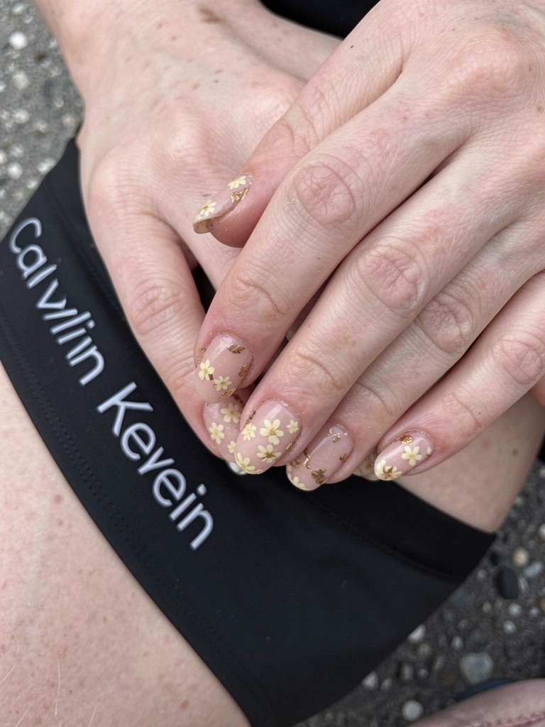Mãos femininas com unhas decoradas em tons de prata e azul, com detalhes brilhantes e strass, sobre fundo neutro.