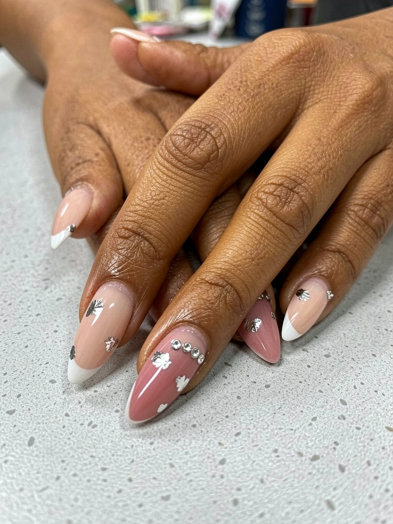 Unhas de gel nude com pedrarias prateadas aplicadas sobre as cutículas.